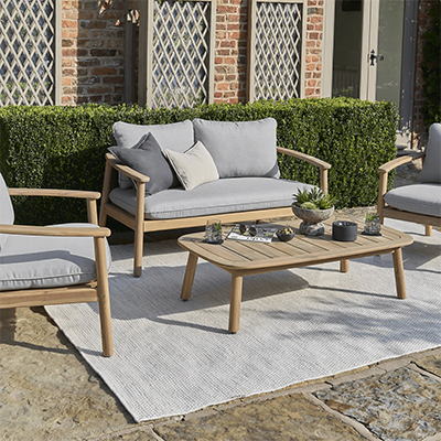Studio image of Kettler Freeport Lounge Set, with a 2 seat sofa and 2 lounge chairs with weave backs with cushions in a grey colourway, with a wooden frame, and a wooden coffee table