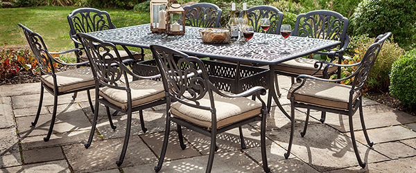 Hartman Amalfi 8 Seat Dining Set in Bronze / Amber on a patio surrounded by shrubs and lawn
