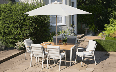 LG Lisbon 6 seat dining set, with cream metal chairs and wooden style slatted table top, and parasol, on a patio in a garden