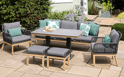 Capri Lounge Set with 2-seat sofa, 2 chairs and a coffee table, with grey cushions and a grey frame, on a stone patio in a garden