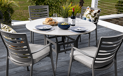 Hartman Lyra 4 Seat Dining Set positioned on a wooden patio with a wood clad house in background.