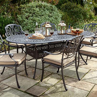 Image of Hartman Amalfi 6 seater dining set with oval table with a bronze toned metal frame and amber coloured seat cushions, in a garden setting