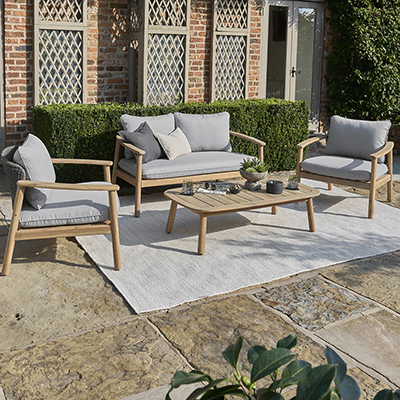 Studio image of Kettler Freeport Lounge Set, with a 2 seat sofa and 2 lounge chairs with weave backs and cushions in a grey colourway, with a wooden frame, and a wooden coffee table