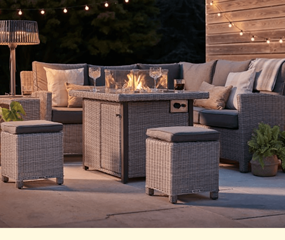 Image of a Kettler corner set at night with decorative lights in the back ground, a kettler heater to one side and its firpit table alight with drinks around it - an item available in our range of weave garden furniture