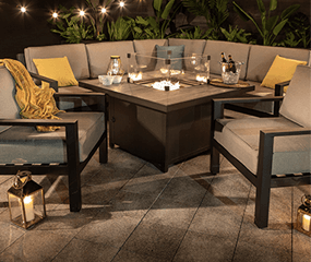 Image of an apollo corner set at night with it's firepit table alight and bottles in ice bucket to one side of the table - an item available from our metal garden furniture range